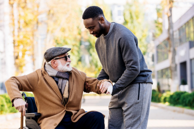 young african american helping disabled senior man to get up from wheelchair