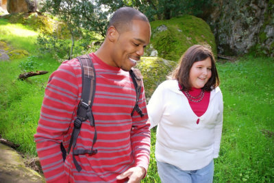 young man and a visually impaired woman walking through a forest