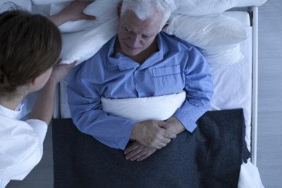 caregiver taking care of disabled senior man in bed